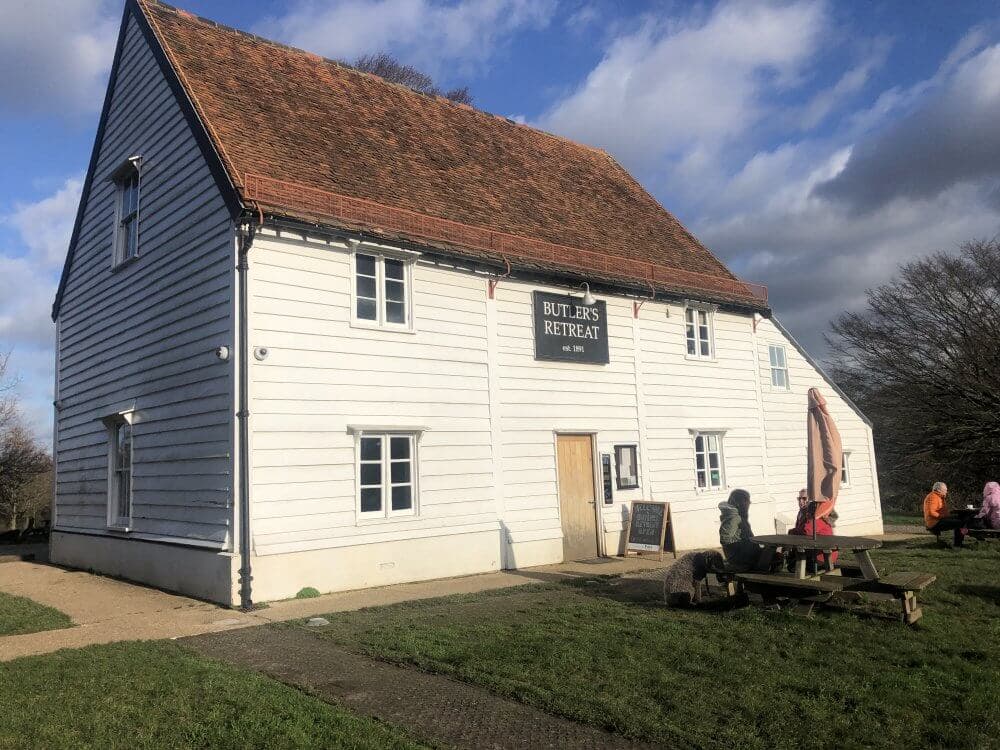 A white wooden building with a sign reading "Butler's Retreat" and people sitting on picnic tables outside. - Home Instead