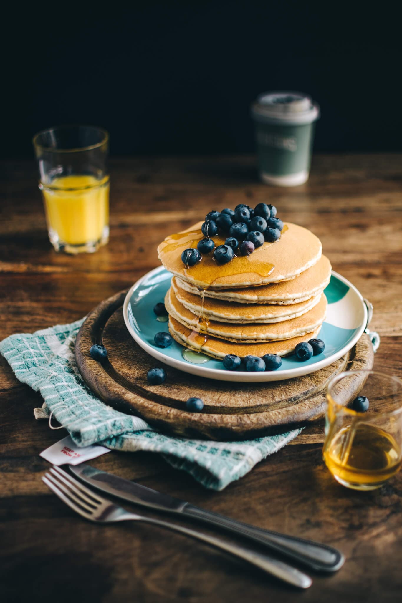 A stack of pancakes topped with blueberries and syrup, surrounded by breakfast items on a wooden table. - Home Instead