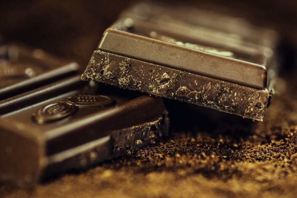 Close-up of two pieces of dark chocolate with detailed texture, laid on a dark surface. - Home Instead