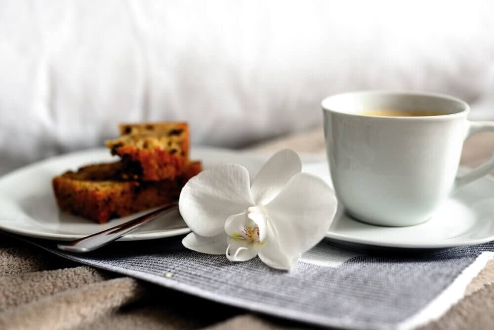 A cup of coffee with two slices of bread on a plate, garnished with a white orchid on a textured surface. - Home Instead