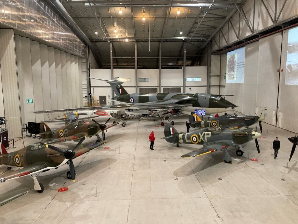 Aviation museum hangar showcasing vintage military aircraft with people walking around and viewing exhibits. - Home Instead