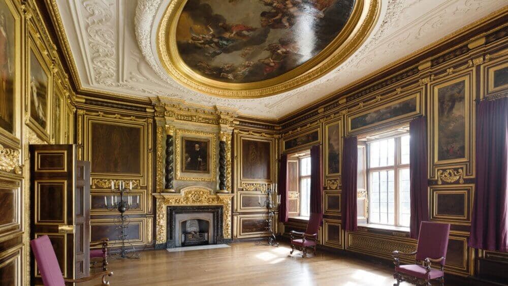 A lavishly decorated room with ornate gold-trimmed walls, a fireplace, and an elaborate ceiling mural. - Home Instead