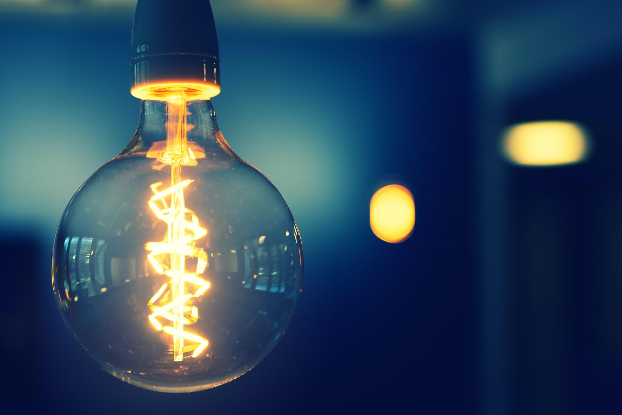 Close-up of an illuminated light bulb with a visible filament against a dark blurred background. - Home Instead