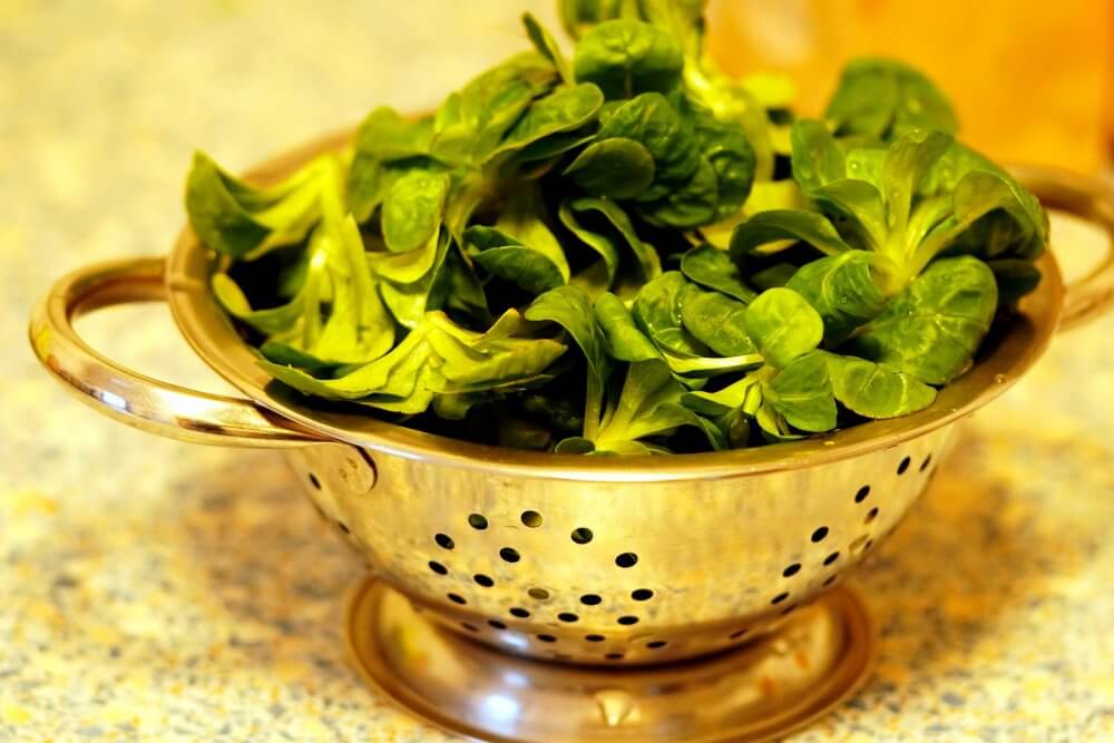 Fresh spinach leaves in a metal colander on a speckled countertop. - Home Instead