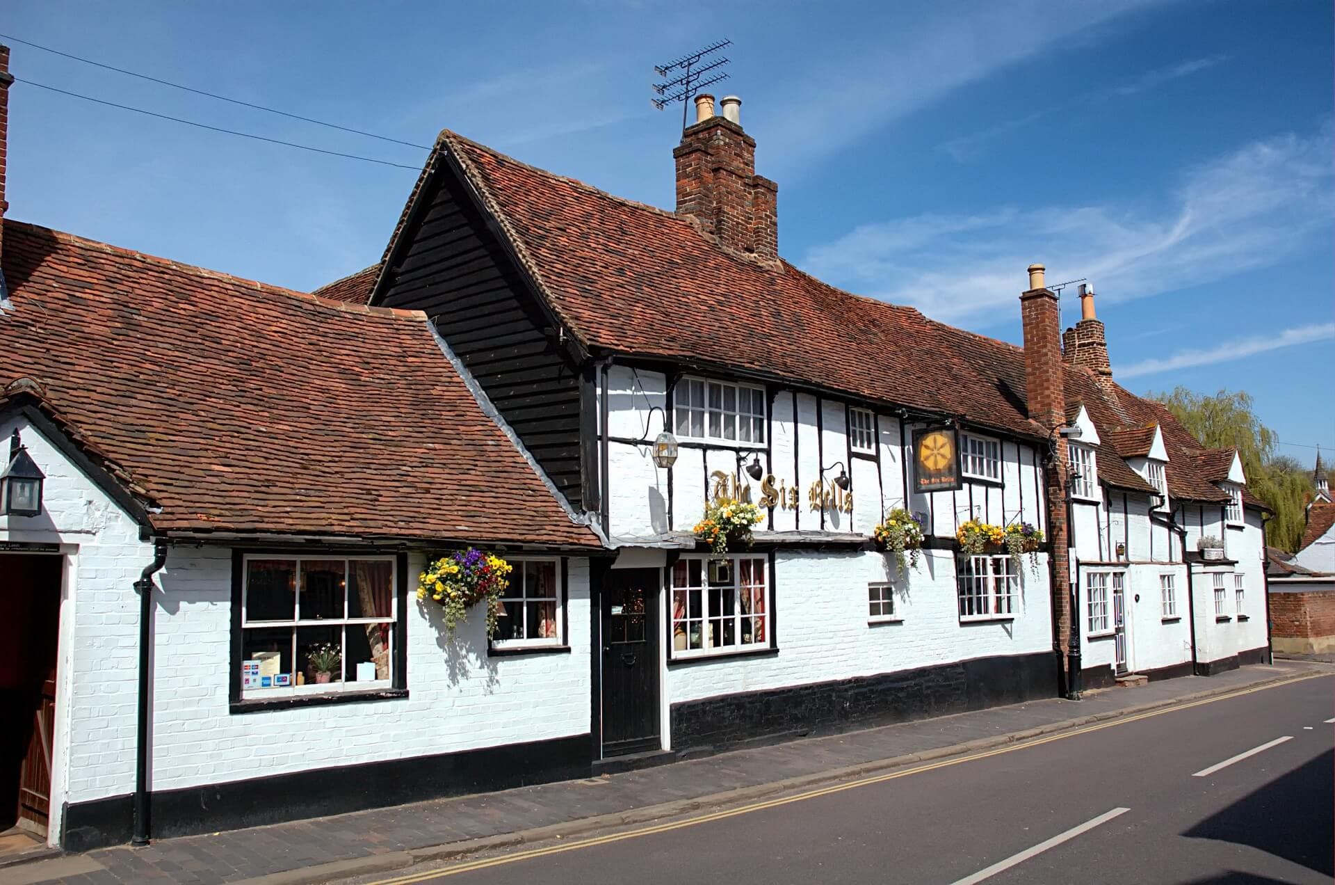 A traditional white-painted English pub with hanging flower baskets and a red-tiled roof on a sunny day. - Home Instead