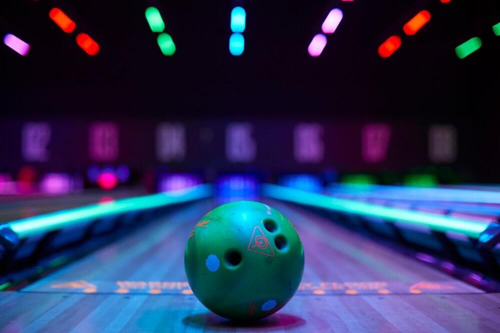 Green bowling ball on a lane under vibrant neon lights in a bowling alley. - Home Instead