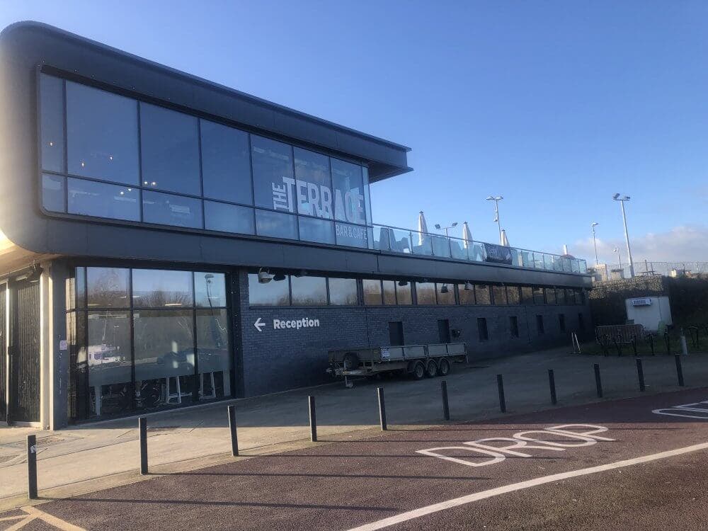 Two-story modern building with glass windows and a sign that reads "The Terrace." The ground floor has a reception arrow. - Home Instead