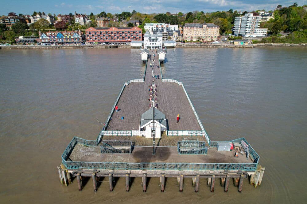 Aerial view of a long pier extending into a body of water, with people walking and buildings in the background. - Home Instead