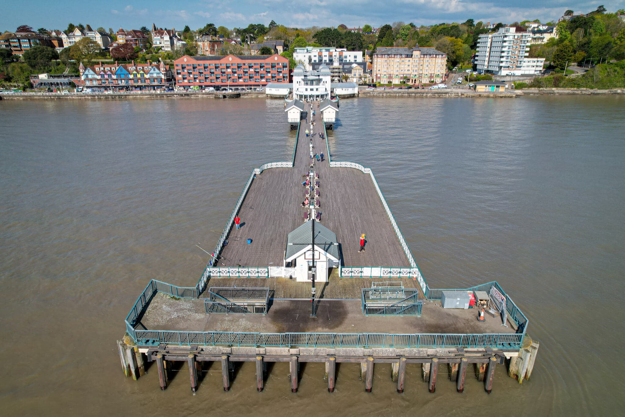 Aerial view of a long pier extending into a body of water, with people walking and buildings in the background. - Home Instead