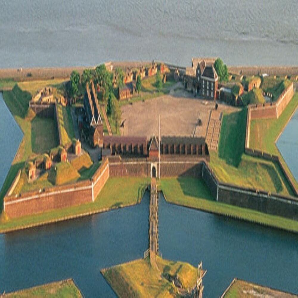 Aerial view of a star-shaped fort surrounded by water with green lawns and brick buildings inside. - Home Instead
