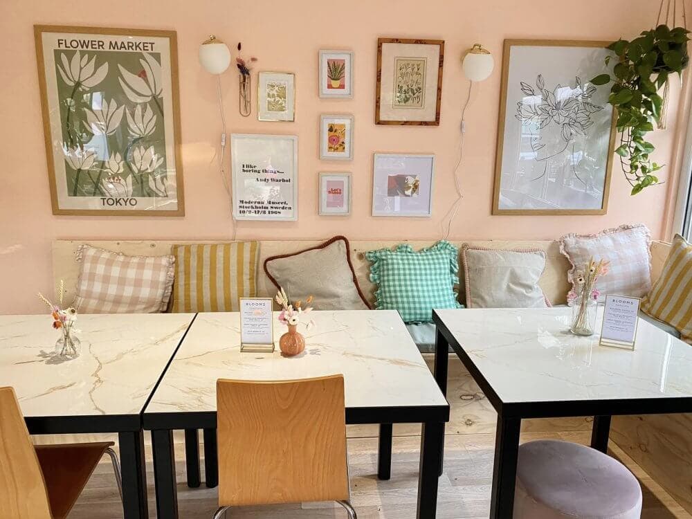 Cozy café with framed art on the wall, three tables with marble tops, and a mix of chairs and cushions. - Home Instead