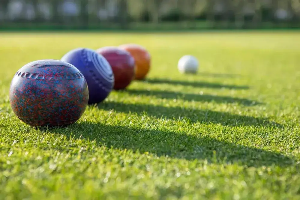 Close-up of several colorful bocce balls lined up on green grass with a white target ball in the distance. - Home Instead