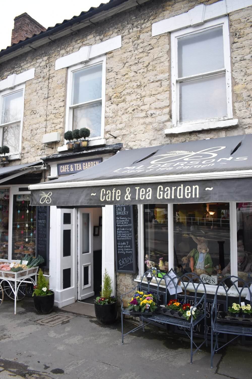 A stone building with a "Cafe & Tea Garden" sign above the entrance and outdoor seating in front. - Home Instead