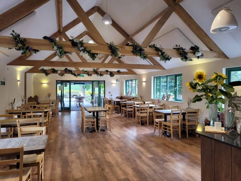 Bright dining room with wooden beams, decorated with flowers and sunflowers, featuring wooden tables and chairs. - Home Instead