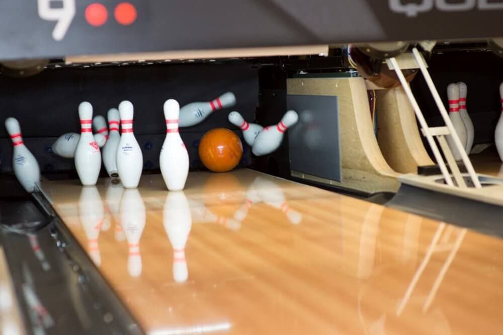 A bowling ball hitting pins in a bowling alley, with pins falling and some standing. - Home Instead