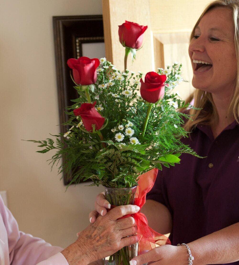 Home Instead Basingstoke picture of a smiling woman from Buds Floristry handing over a vase of red roses to a client