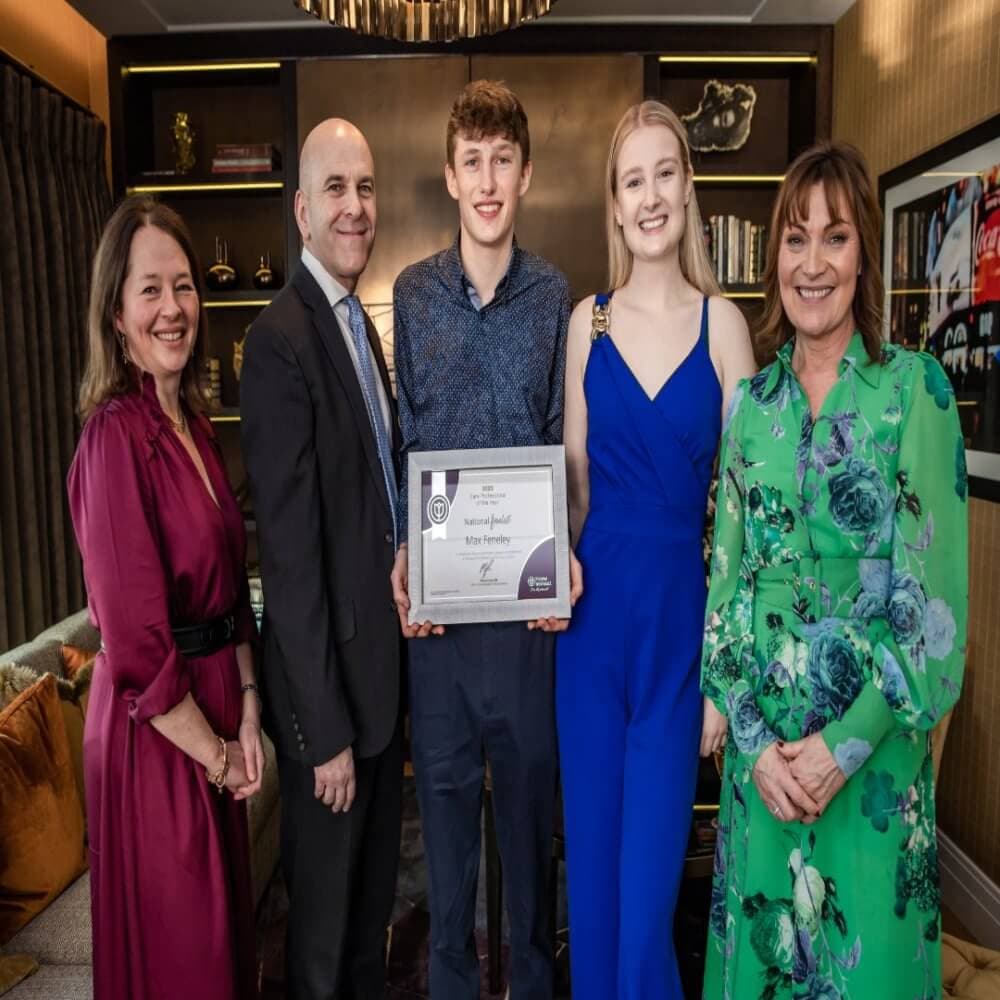 Five people posing, with a young man in the center holding a certificate, in a well-lit, elegant room. - Home Instead