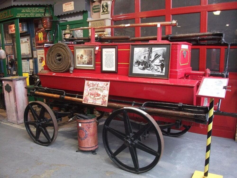 Vintage red fire engine on display with historical photos, hose, and informational posters in a museum setting. - Home Instead