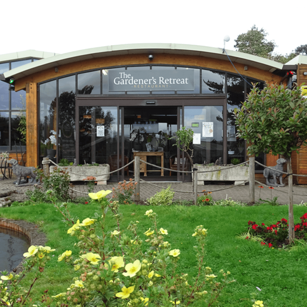 Entrance to The Gardener's Retreat restaurant with surrounding greenery and a small pond in front. - Home Instead