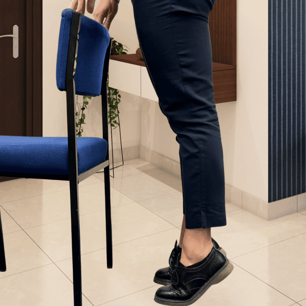 A person lifting a blue chair with one hand, showing only legs and feet in black shoes. - Home Instead