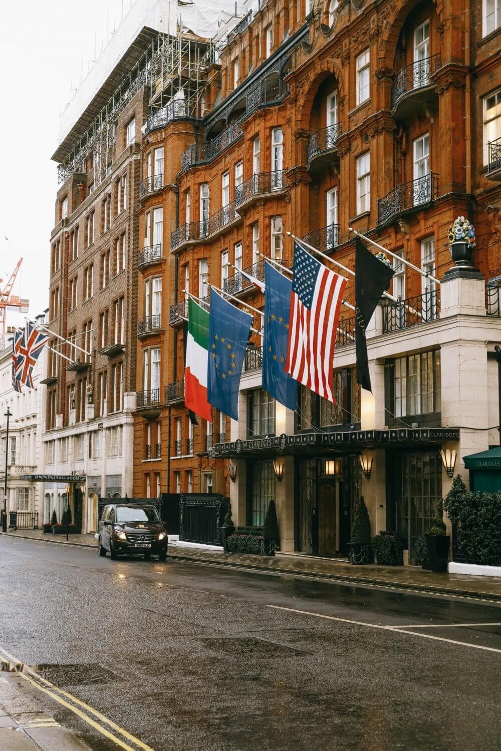 Brick building with flags of different countries on a wet street with a black car passing by. - Home Instead