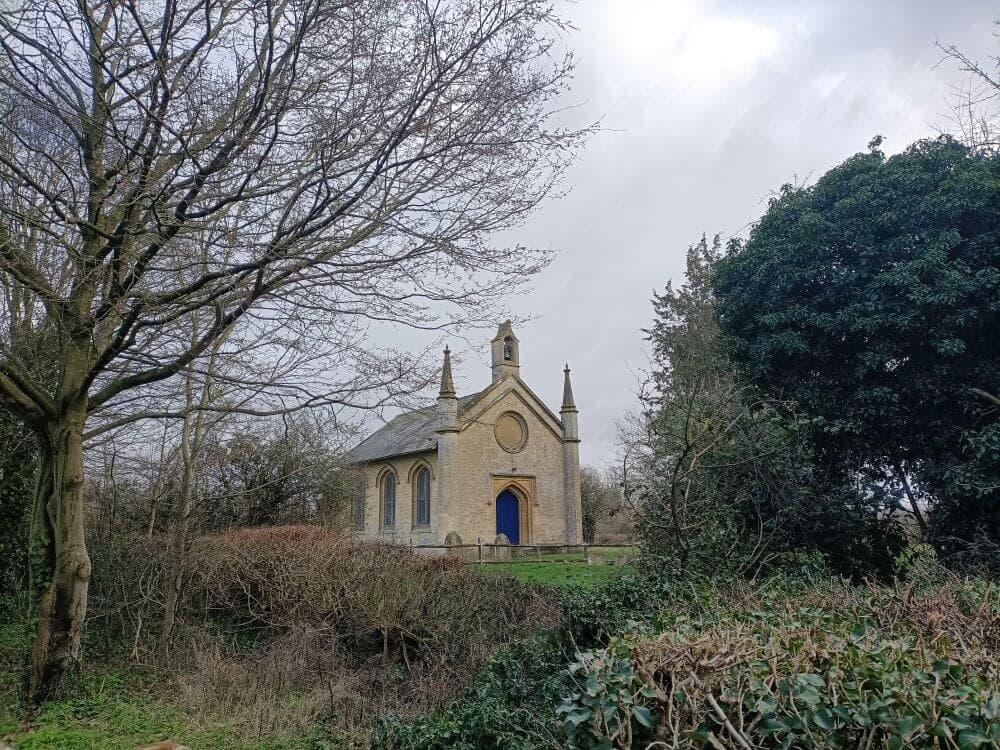 A quaint, small church with a blue door, surrounded by trees and shrubs on a cloudy day. - Home Instead