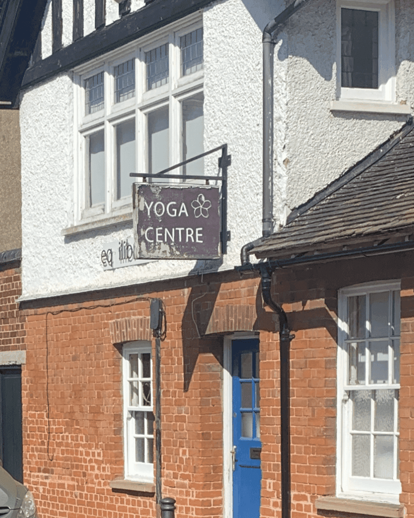 A building with a red brick exterior and sign reading "Yoga Centre" hangs near the blue door. - Home Instead