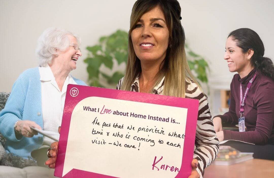 A smiling woman holds a sign. Behind her, two women, one elderly and one younger, chat. The sign reads, "Karen. - Home Instead