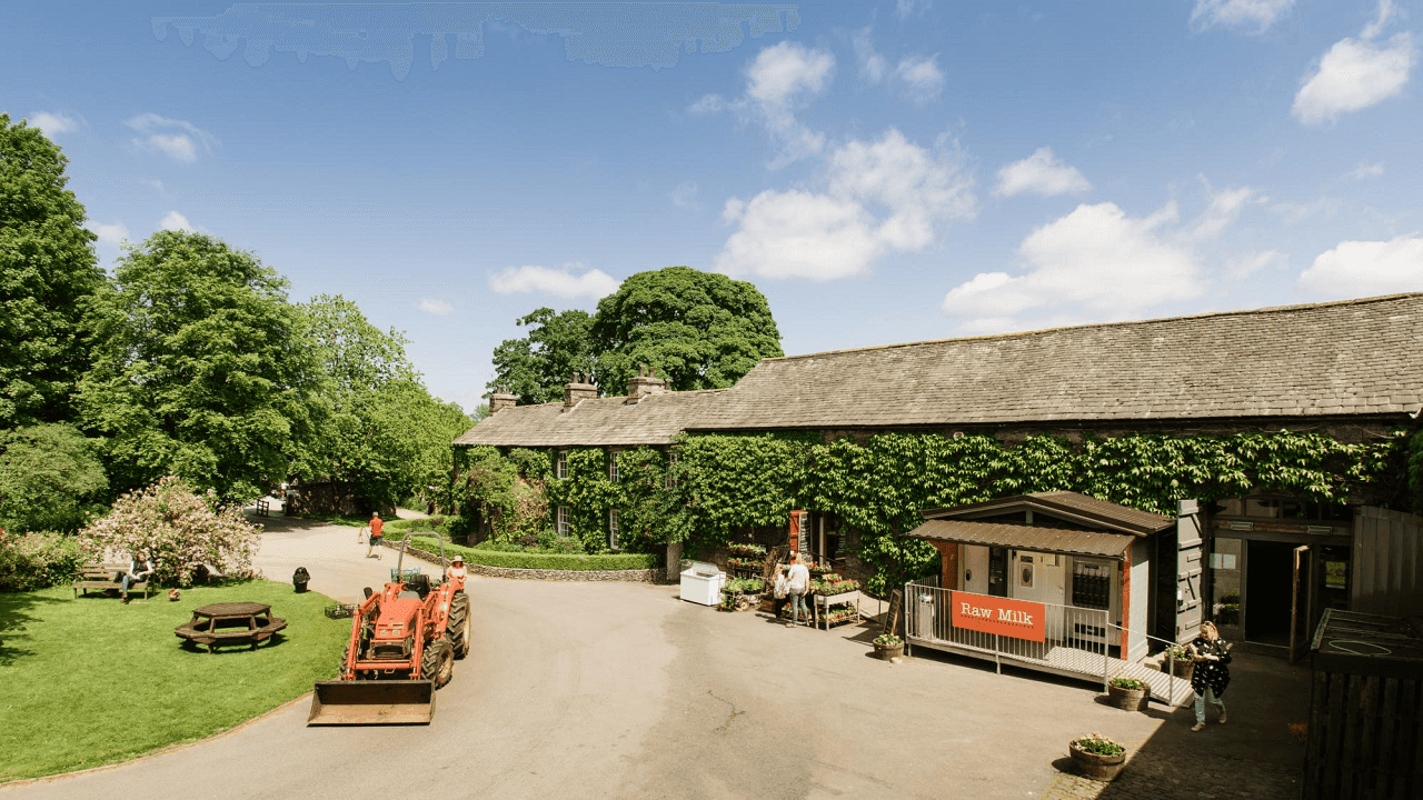 Tractor near a building with a "Raw Milk" sign, surrounded by trees and greenery, with people sitting outside. - Home Instead