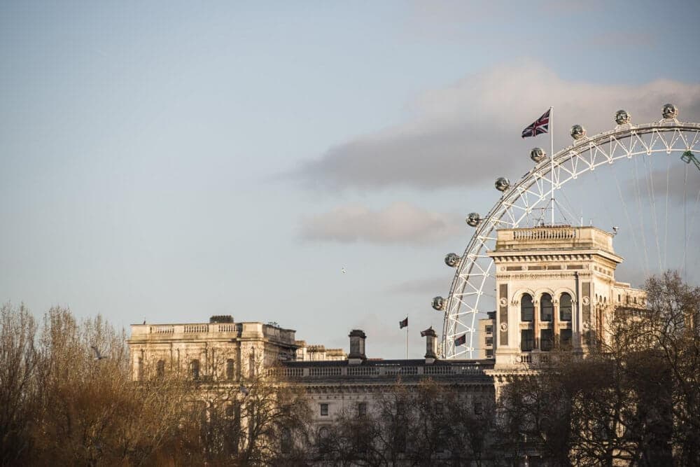 A historic building with a Union Jack and part of the London Eye visible against a blue sky with light clouds. - Home Instead