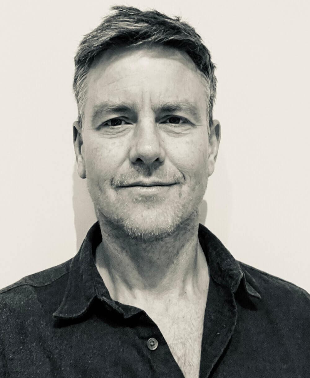 A black-and-white photo of a man with short hair, wearing a button-up shirt, and looking directly at the camera. - Home Instead