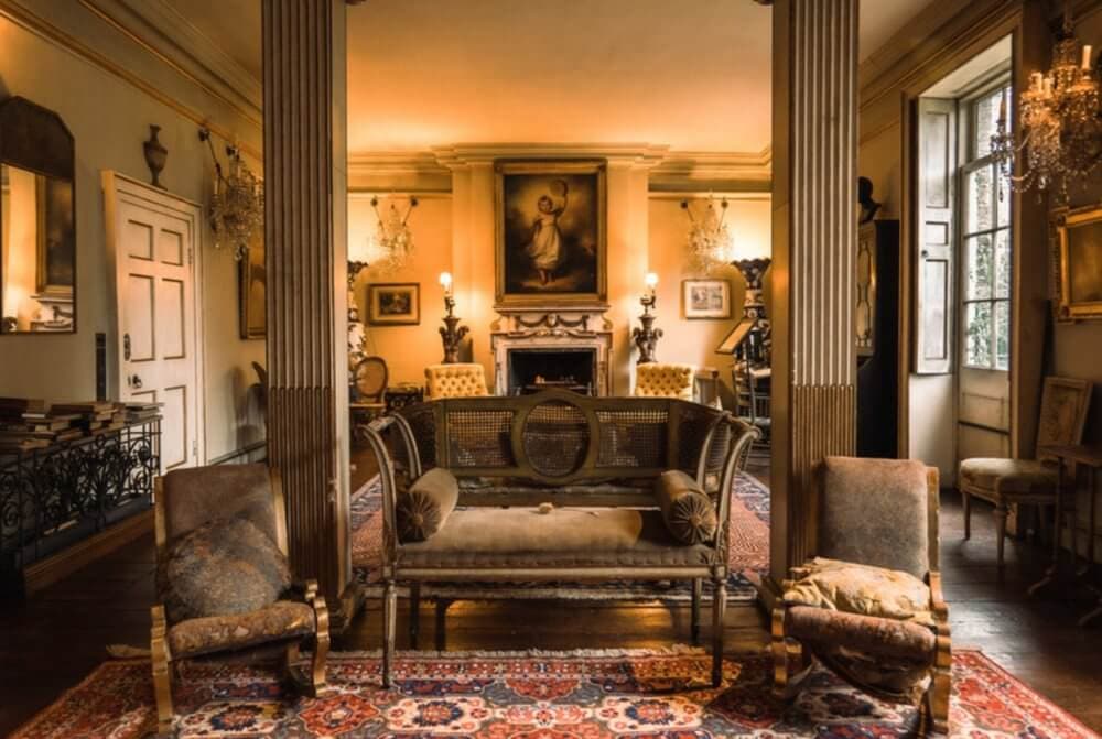 Elegant vintage living room with ornate furniture, chandeliers, a large framed portrait, and Persian rugs. - Home Instead