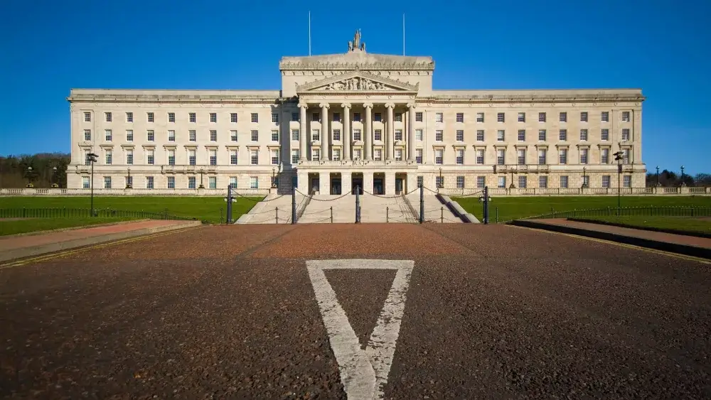 Front view of the neoclassical Parliament Buildings in Belfast, a large white structure with columns and a triangular pediment. - Home Instead