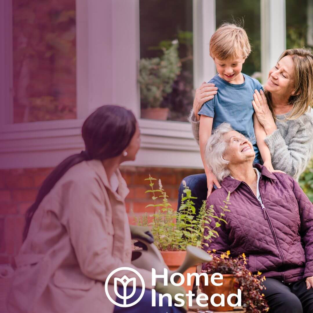 Three generations of a family smiling and interacting on a porch, with a "Home Instead" logo in the lower left corner. - Home Instead