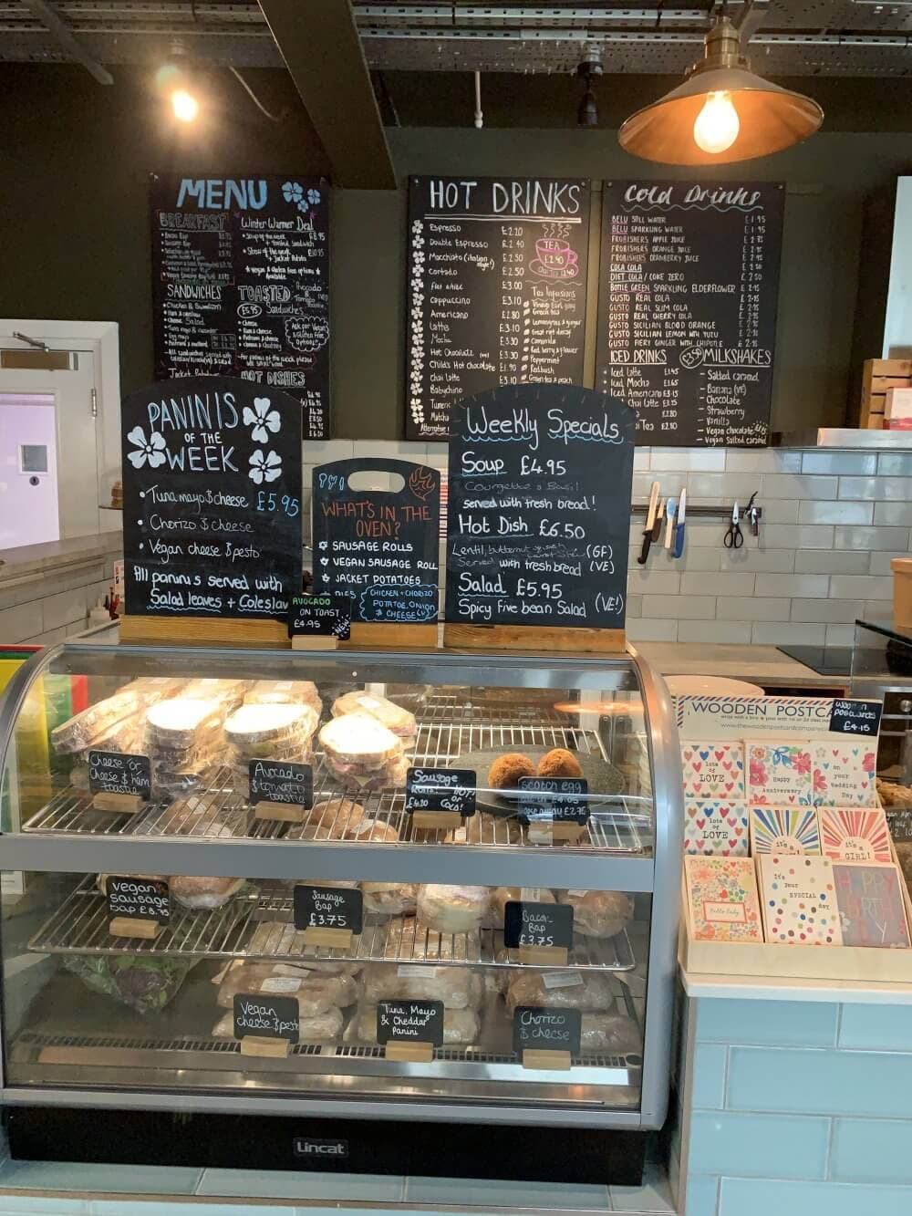 Home Instead Basingstoke picture of the food counter at The Honesty Cafe showing a variety of sandwiches and pastries, with chalkboard menus and weekly specials on the wall behind.