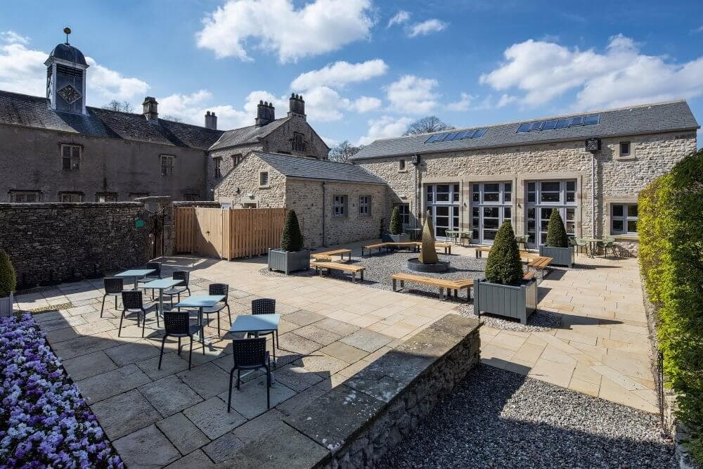 Stone patio with chairs, tables, and potted plants, adjacent to a stone building under a partly cloudy sky. - Home Instead