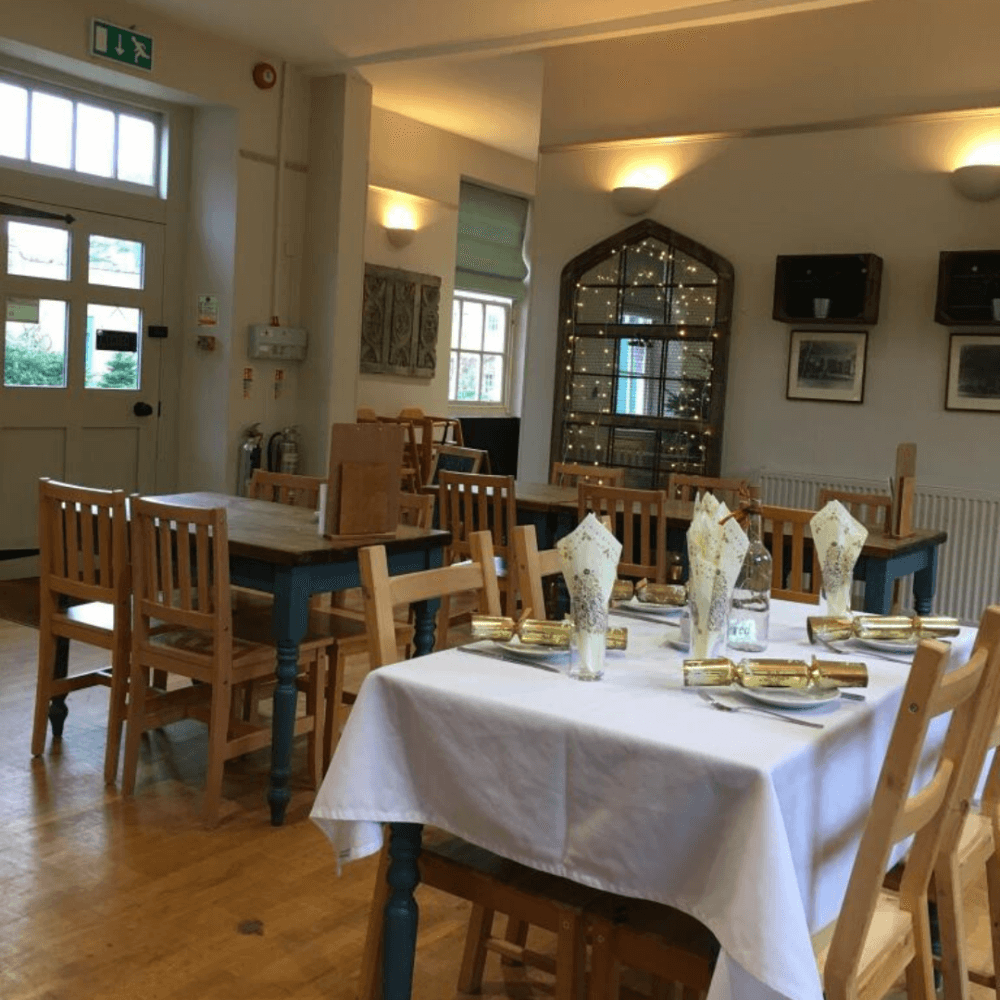 A cozy dining room with wooden furniture, a fully set white table, and a decorative cabinet with lights in the background. - Home Instead
