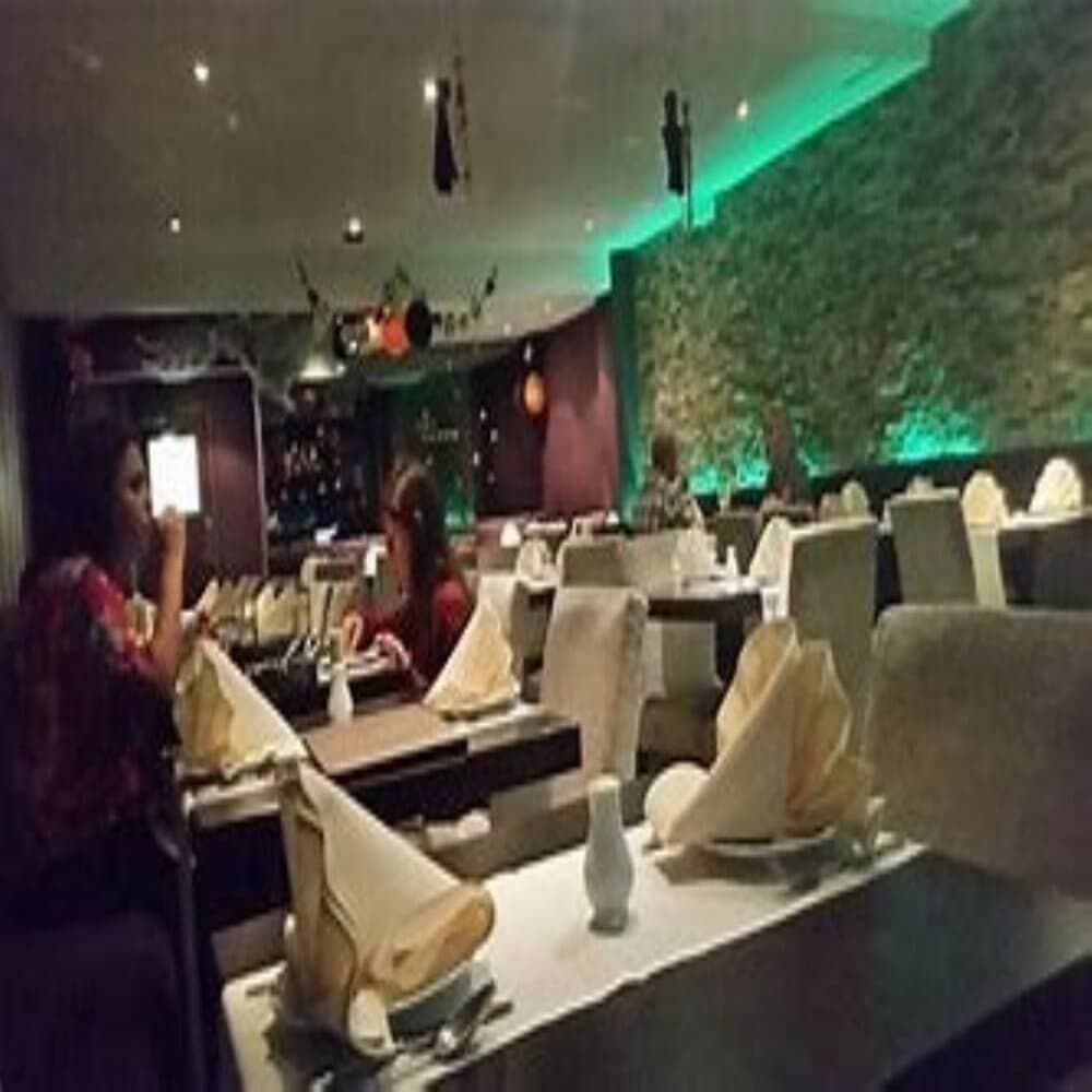 A dimly lit restaurant with stone walls, green lighting, and tables set with folded napkins; a few diners are seated. - Home Instead