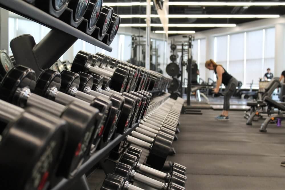Person working out in a gym with rows of dumbbells and other gym equipment in the foreground. - Home Instead