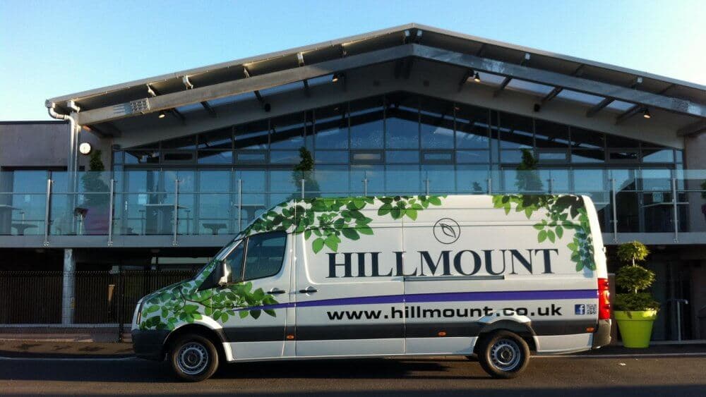 A Hillmount delivery van parked in front of a modern building with large glass windows and a metal roof. - Home Instead