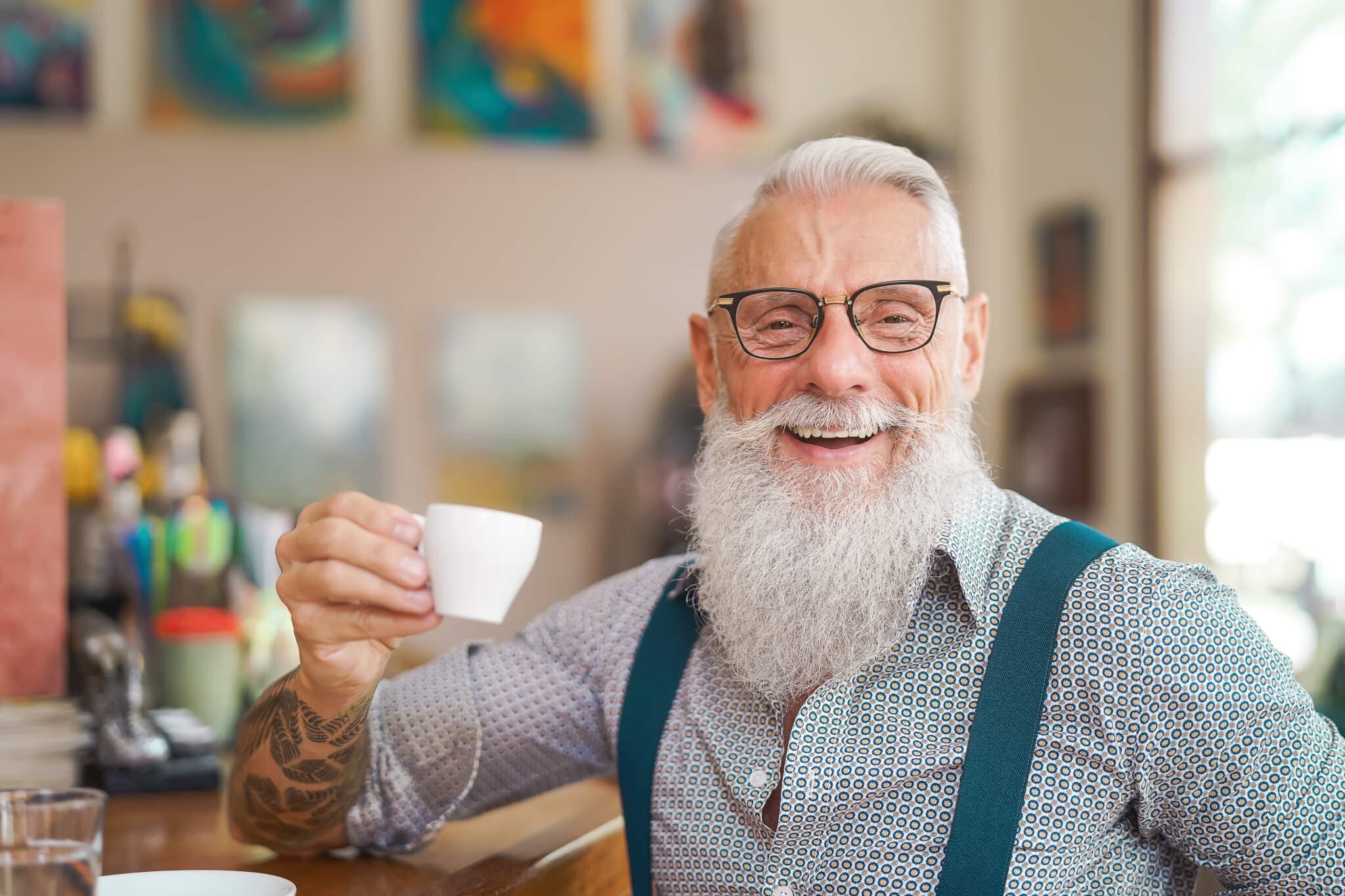 Smiling elderly man with a white beard holding a cup of coffee in a casual setting. - Home Instead