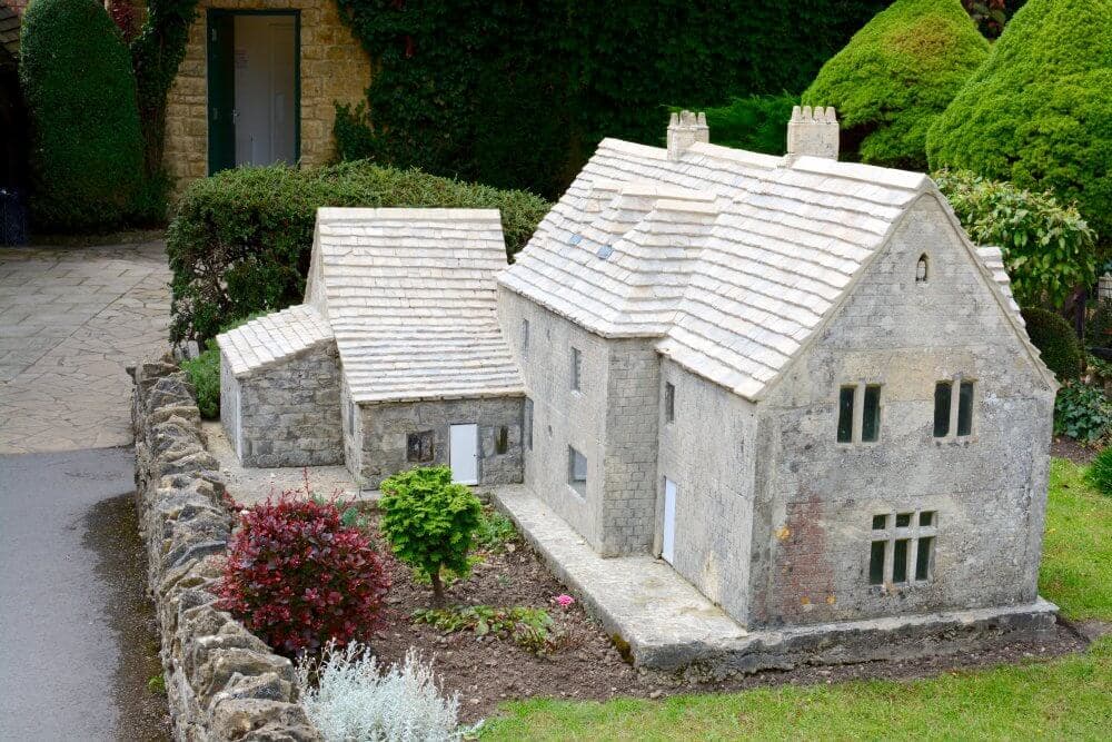 Miniature stone houses with rustic details surrounded by lush greenery and shrubs. - Home Instead