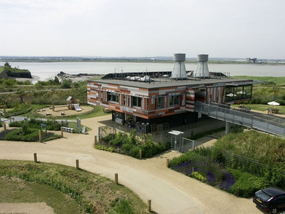 Modern building on stilts with striped exterior, surrounded by green grounds and overlooking a body of water. - Home Instead
