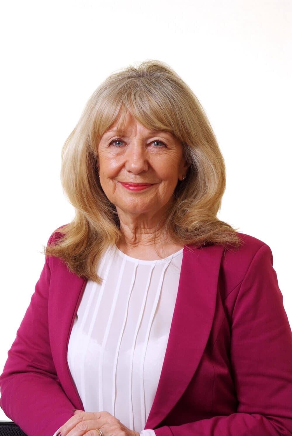 A woman with long blonde hair wearing a magenta blazer and white blouse smiling against a white background. - Home Instead