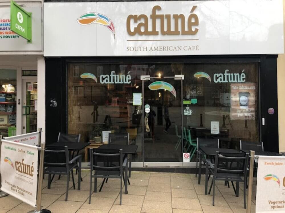 Facade of Cafuné, a South American café, with outdoor seating and signs for fresh juice and vegetarian options. - Home Instead