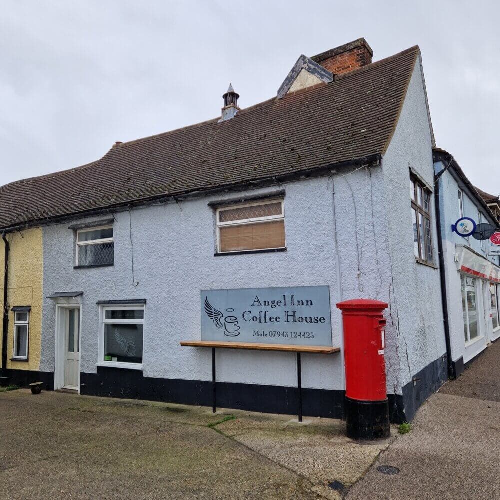 A light blue building with a sign reading "Angel Inn Coffee House." A red postbox stands nearby. - Home Instead