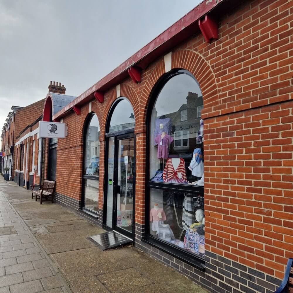 A brick building with arched windows displays clothes. The sidewalk is wet, and the sky appears cloudy. - Home Instead