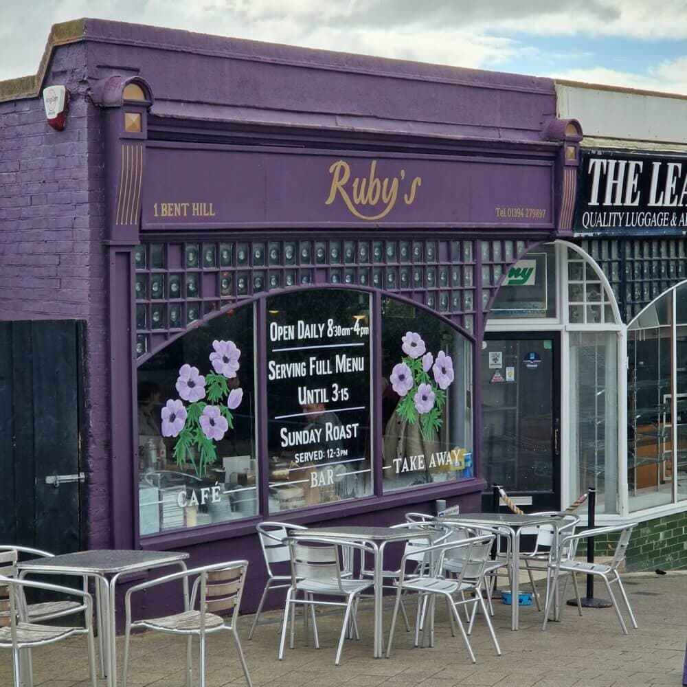 Exterior of Ruby's café with outdoor seating, purple facade, and flowers painted on the windows. - Home Instead