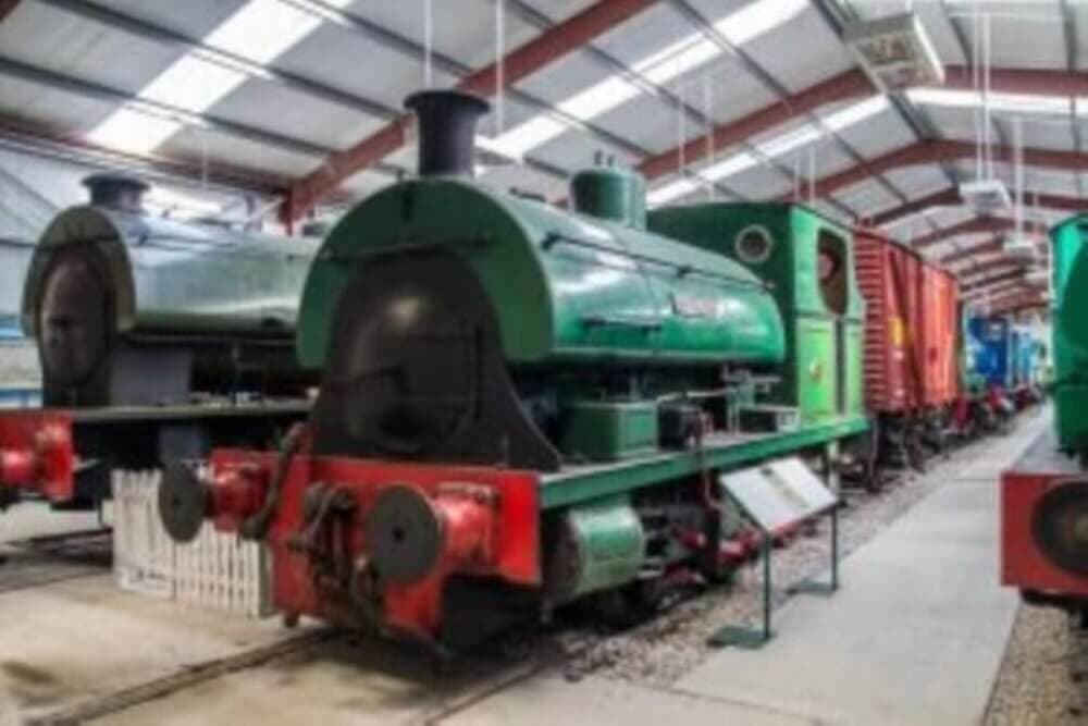 A row of vintage steam locomotives on display indoors at a train museum. - Home Instead