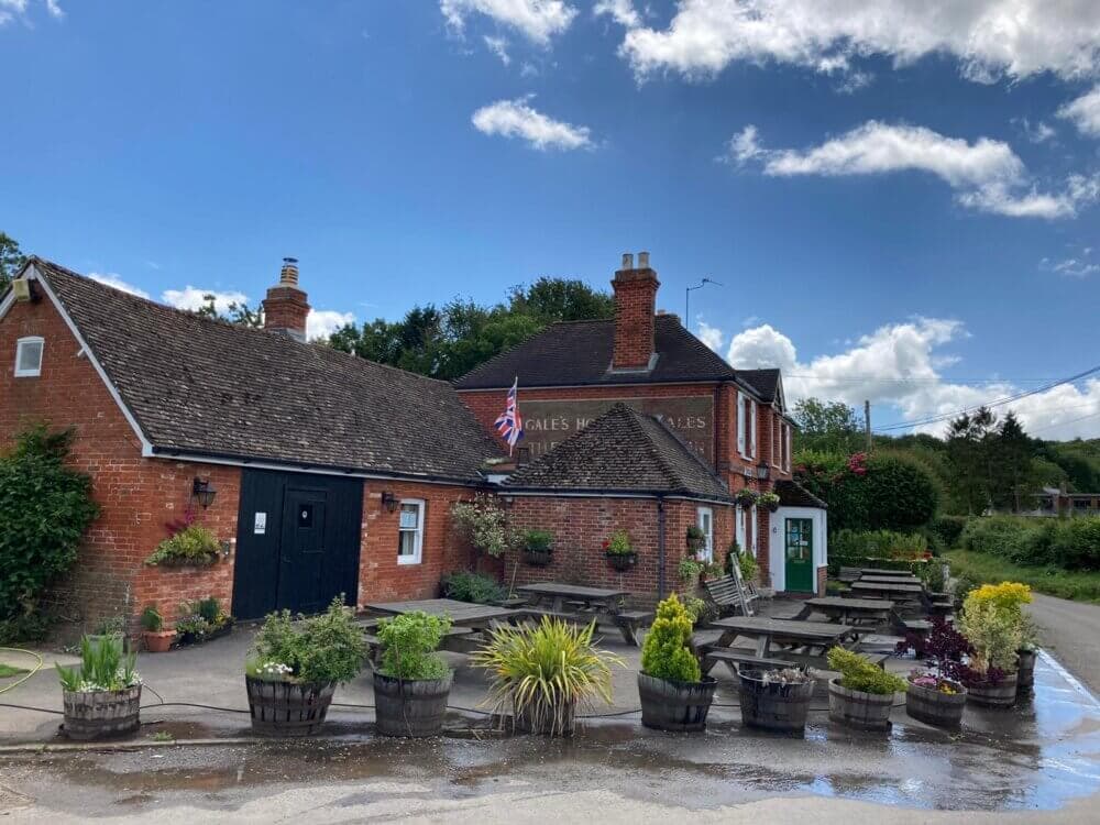 A quaint brick pub with outdoor seating, lush plants in pots, and an American flag on a sunny day. - Home Instead